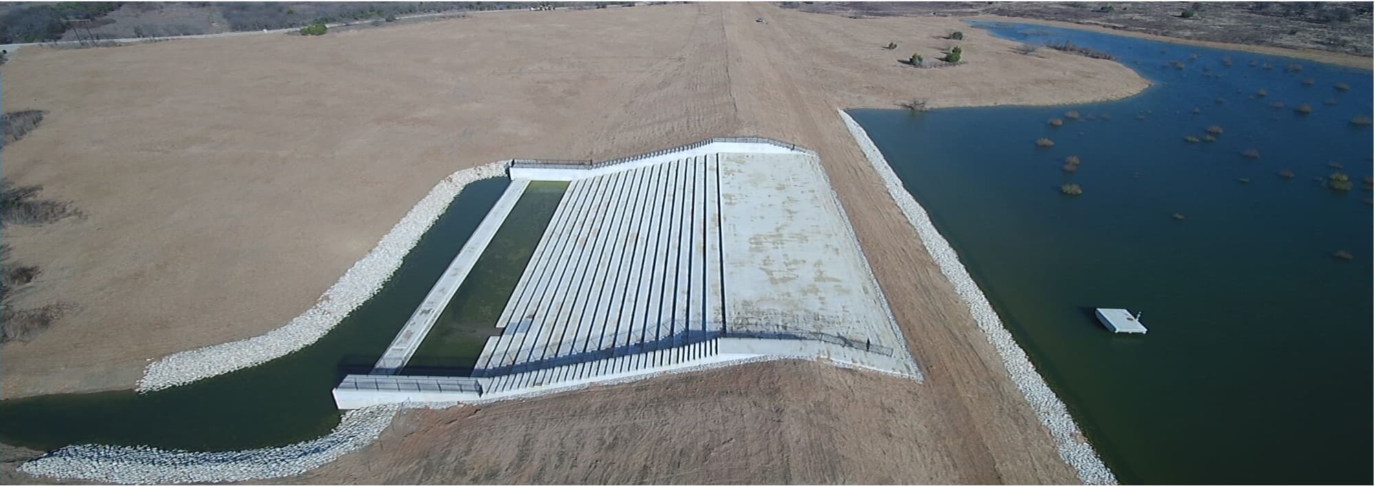 Aerial view of a newly rebuilt concrete stepped spillway between two arms of a reservoir.