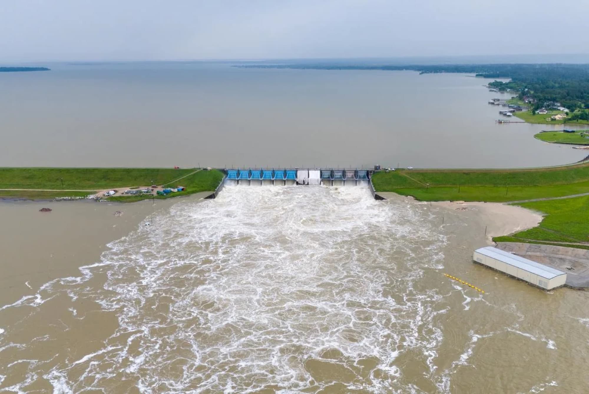 Aerial view of a gated spillway discharging at full flow below a large reservoir.